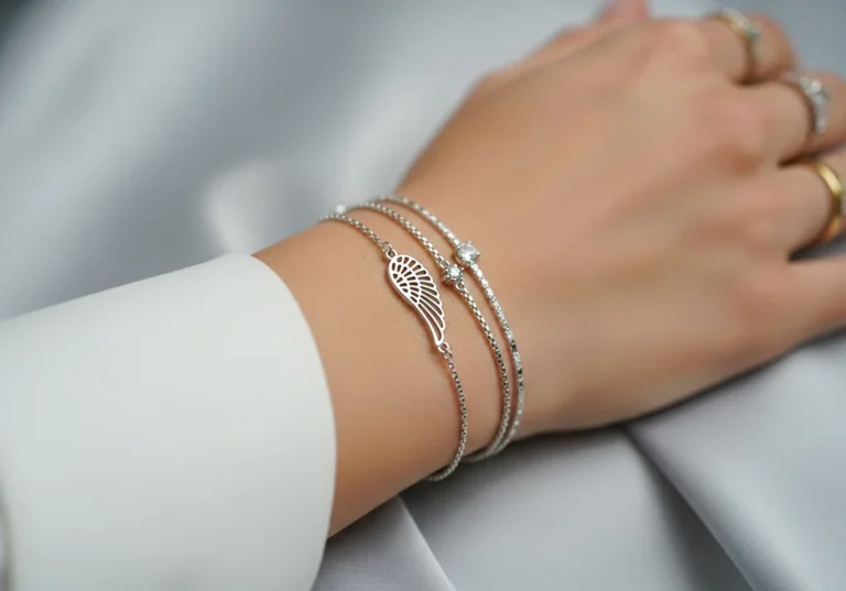 Kobiecy nadgarstek z warstwowymi, srebrnymi bransoletkami; jedna z filigranowym skrzydłem, pozostałe z kryształkami.